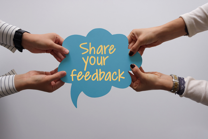 Sign with words Share Your Feedback and two hands holding the sign on either sign