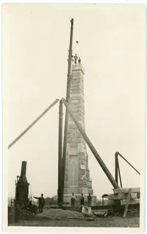 Old black and white picture, with people around and on top of the war memorial tower under construction