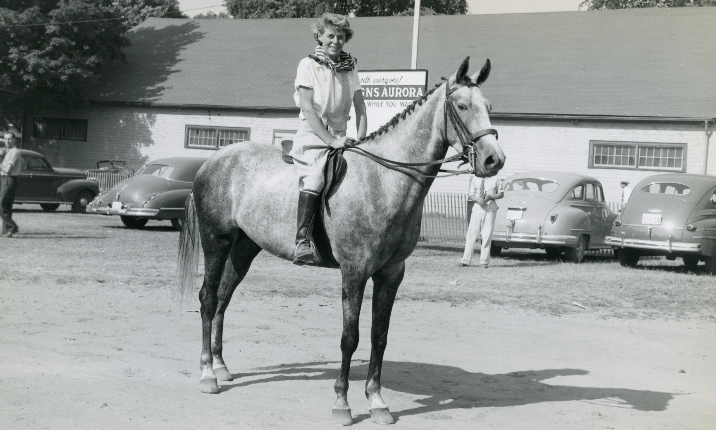 "A black and white image of a woman on top of a horse, participating in the Aurora Horse Show, Town Park, 1948."